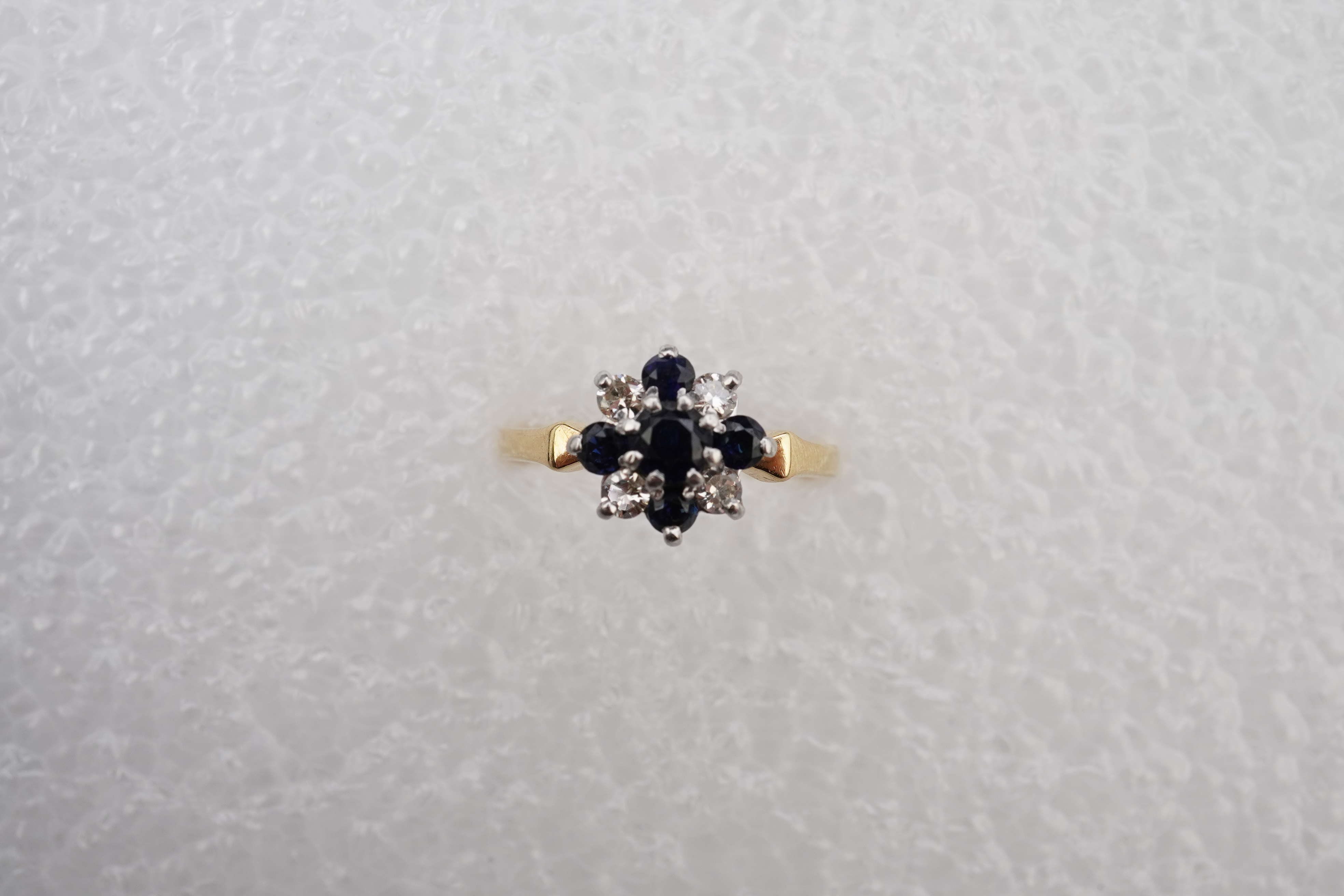 A sapphire and diamond cluster ring, set with circular-cut sapphires and brilliant-cut diamonds totalling approximately 0.20 carats, mounted in gold and platinum, size M, stamped 18CT PLAT, gross weight approximately 3.5